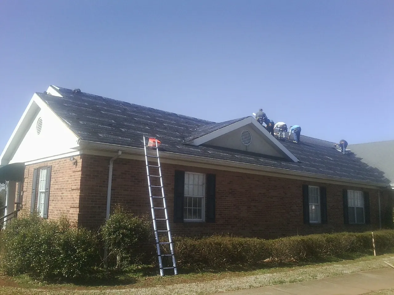 Crew tearing shingles off a brick ranch roof with a ladder set — Emergency Roof Repair work by our crew in Buchanan