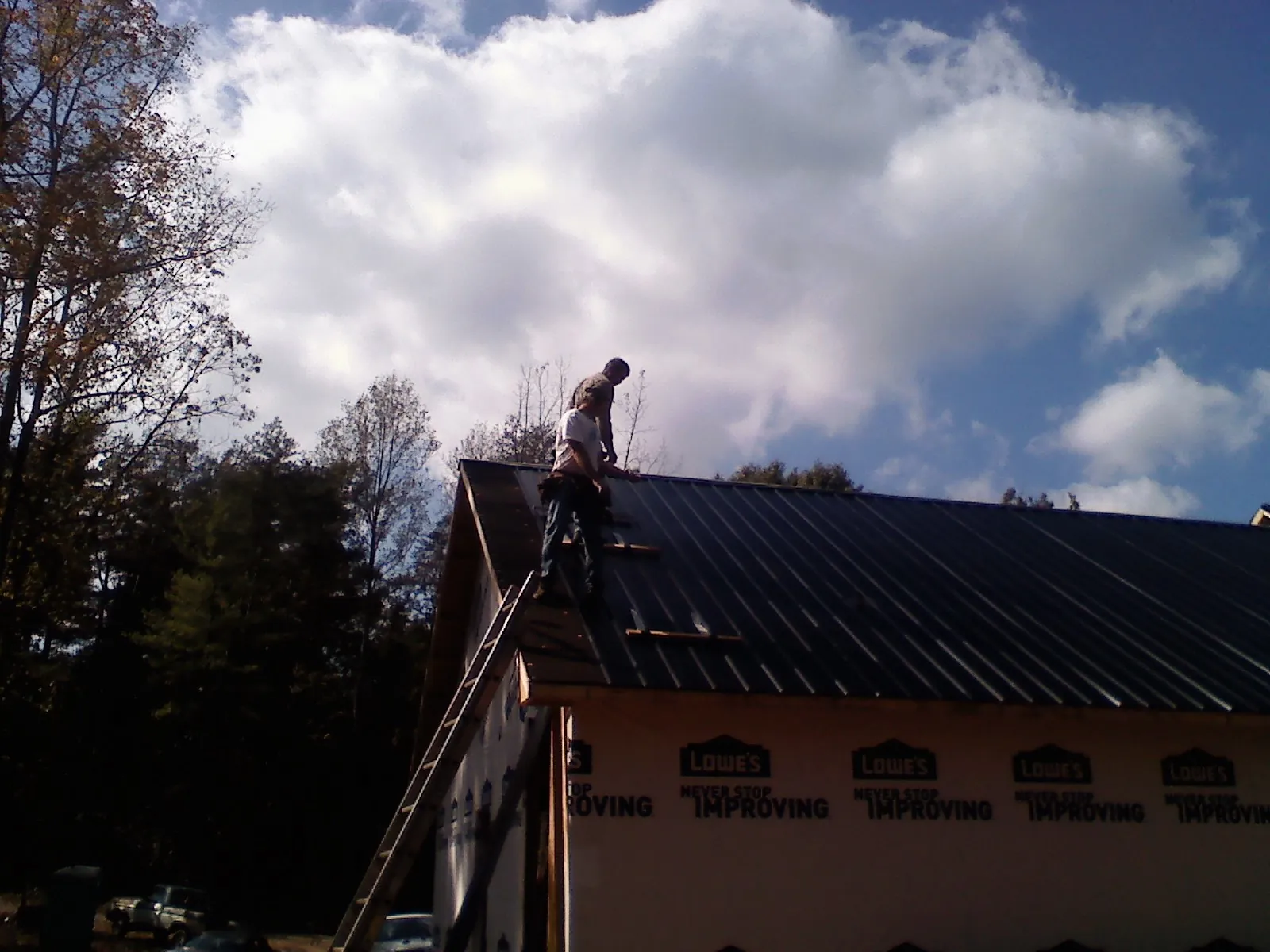 Roofer fastening dark metal panels high against a cloudy sky, from a Roof Inspection job in Buchanan